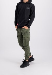 Felpa nera con cappuccio e tasca frontale, pantaloni cargo verde oliva con tasche laterali e scarpe da ginnastica nere con lacci.