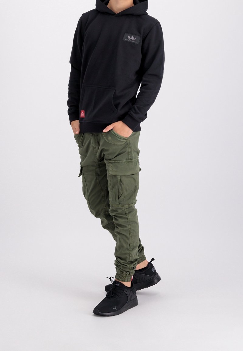 Felpa nera con cappuccio e tasca frontale, pantaloni cargo verde oliva con tasche laterali e scarpe da ginnastica nere con lacci.