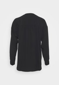 Maglietta nera a maniche lunghe con un tessuto liscio e fluido. Presenta un retro plissettato e polsini con bottoni. Design semplice e monocolore.
