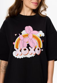 Zwarte oversized t-shirt met een roze ballondog graphic, regenboogontwerp en "XOXO" tekst in gestileerde witte letters met wolkaccenten.