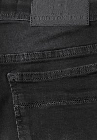 Svart denim med en slät yta, med en rektangulär läderlapp märkt "STREET ONE MEN" och tonad sömnad.