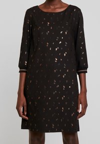 Robe noire à manches trois-quarts, ornée d'un motif floral métallique en or et en bronze. Tissu lisse et décolleté bateau.