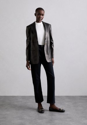 Blazer de cuero negro sobre una blusa blanca, combinado con jeans rectos de color azul oscuro y flats negros con acentos dorados. Atuendo simple y moderno.