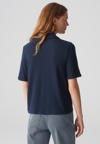 Polo shirt blu navy con maniche corte, colletto e polsini arrotolati; texture morbida e vestibilità su misura abbinata a pantaloni a righe.