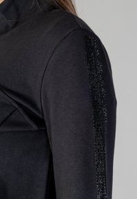 Felpa nera con colletto alto e un accentuato motivo testurizzato e perlato lungo il braccio. Il tessuto è liscio con un design aderente.