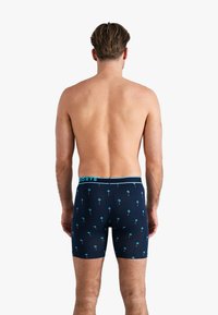 Navyblauwe boxershorts met een patroon van kleine palmbomen, met een lichtblauwe tailleband met de tekst "SHORTS." Zachte stof, aansluitend ontwerp.