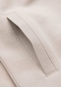 Tissu beige en gros plan montrant un bord côtelé d'une petite poche ou pochette cousue sur une surface textile assortie.