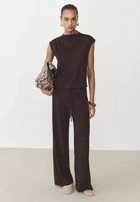 Brown two-piece outfit featuring a sleeveless top with a high neckline and loose-fitting pants with a drawstring, complemented by a snake-print clutch.