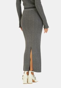 Falda midi gris de canalé con abertura lateral, adornada con acentos metálicos. Combinada con zapatos de tacón cuadrado blancos que presentan elementos decorativos.