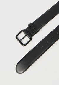 Μαύρη δερμάτινη ζώνη με μαύρη μεταλλική αγκράφα και πολλαπλές τρύπες ρύθμισης σε ανοιχτό φόντο.