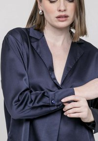 Chemise en satin bleu marine avec un col, des poignets à boutons et une texture lisse. Présente une coupe décontractée avec un décolleté en V profond.