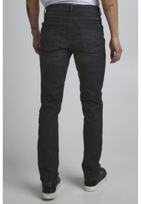 Dark denim jeans with a slim fit, featuring standard back pockets, a mid-rise waist, and a slightly textured surface. Worn with black sneakers.