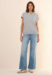 Striped short-sleeve top with a V-neck, paired with light blue wide-leg jeans and grey sneakers with a beige accent.