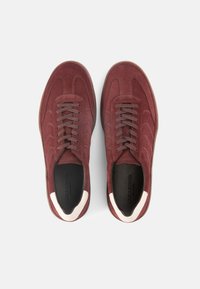 Μπορντό σουέντ αθλητικά παπούτσια με γκρι κορδόνια και λευκή διακριτική λεπτομέρεια στον αστράγαλο. Διαθέτουν καμπυλωτές ραφές και υφασμένη ελαστική σόλα.