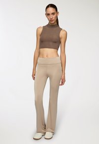 Top corto marrone senza maniche abbinato a pantaloni flare beige aderenti. Texture liscia, tessuto morbido, senza motivi visibili, accompagnato da sneakers bianche.