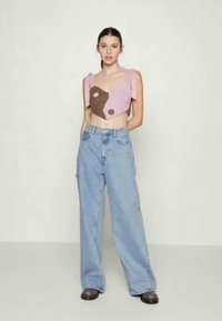 Top de malha cropped com design abstrato em rosa e castanho; combinado com jeans baggy azul claro e sapatos pretos chunky.