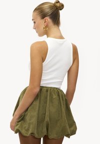 Haut blanc sans manches avec un col rond, associé à une mini-jupe en daim verte avec une taille froncée et une texture superposée.