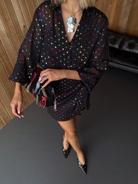 Fekete áttetsző ruha színes pöttyökkel, túlméretezett ujjakkal, fémes nyaklánccal és texturált hímzett borítéktáskával. Fekete hegyes orrú cipő.