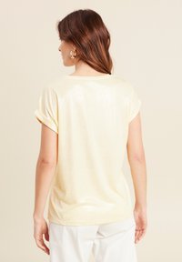 Korte mouwen, lichtgele shirt met een zachte, glanzende textuur. Opgerolde mouwen en een losse pasvorm, zonder zichtbare patronen of hardwaredetails.
