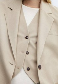 Beige maßgeschneiderter Blazer und Weste, mit einer einzelnen Brusttasche, fünf Knöpfen an der Weste und glattem Stoffgefühl.
