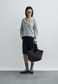 Γκρι πλεκτό πουλόβερ με κουκούλα και κουμπιά, σορτς ναυτικού μπλε, γκρι κάλτσες με ρίγες, μαύρες μπαλαρίνες και πλεκτή μαύρη τσάντα. Απλός και λειτουργικός σχεδιασμός.