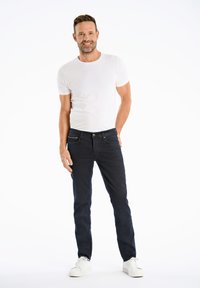 Camiseta blanca de manga corta combinada con jeans azules oscuros y zapatillas blancas. El conjunto presenta un diseño ajustado con una textura suave.