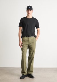 Black t-shirt, olive green pants, black cap with blue logo, and black shoes. The outfit features a relaxed fit and simple design.