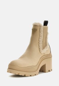Beżowe botki Chelsea z teksturowanym futrzanym kołnierzem, gumową podeszwą i modnie ukształtowanym słupkowym obcasem, z logo po boku.
