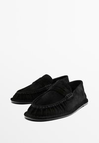 Black suede moccasin shoes with decorative stitching and a fringed detail along the upper edge. Flat rubber sole, slip-on design.