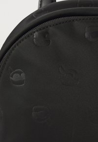 Fekete nylon hátizsák, amelyen diszkrét kidomborodó mintázat található mesefigurákról, lekerekített formával és sima felülettel, fekete varrással.