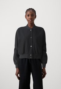Zwarte cropped bomberjack van zachte stof, met een opstaande kraag, drukknoopsluiting en twee Franse zakken met ronde hoeken.