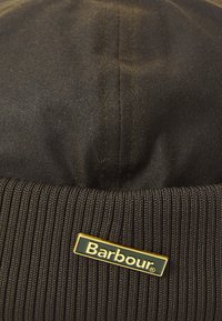 Zwarte beanie met een ribbelstructuurband en een gladde bovenkant. Goudkleurig 'Barbour' logo is aan de voorkant bevestigd ter branding.