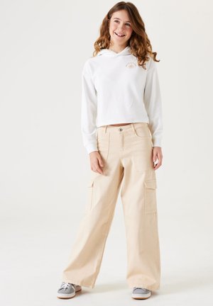 Witte cropped hoodie met een logo aan de voorkant, gecombineerd met beige cargo broeken met grote zijzakken en een relaxed fit, gedragen met grijze sneakers.