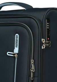Valise de voyage noire avec une surface en tissu texturé, zips argentés et un tirette de zip bleu clair. Dispose d'un cadenas à combinaison sur le côté.