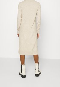 Beige stickad klänning med polokrage, lång ärm och ribbade muddar; kombinerad med vita ankelboots med svarta accent och tjocka sulor.