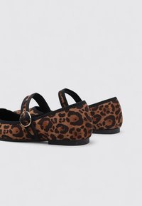 Chaussures plates en imprimé léopard avec accents noirs, dotées d'une sangle avec une boucle dorée. Matériau doux avec un bout arrondi et une semelle basse.