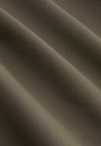 Közeli kép sima, olívazöld szövetről, látható finom átlós szövésmintával és enyhe redőkkel, amelyek lágy árnyékokat hoznak létre.