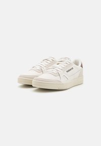 Vita sneakers med ljus beige accenter, gjorda av läder och textil. Har platta snören, perforerad tå och logotypdetalj på sidan.