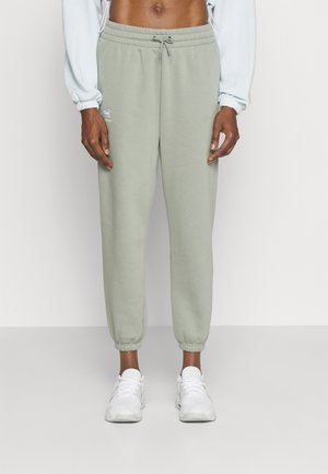 Persoon draagt lichtgrijze joggingbroek met elastische boorden en een tunnelkoord in de taille, gecombineerd met witte sportschoenen.
