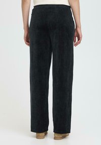 Zwarte corduroy broek met een losse pasvorm, met verticale ribbeltextuur en een tailleband. De zoom is recht en raakt de schoen.
