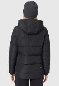 Melnā pūkainā jaka ar quilted dizainu, ar kapuci un piedurknēm ar elastīgu malu. To papildina tumša adīta cepure, kuras tekstūra izceļ siltumu.