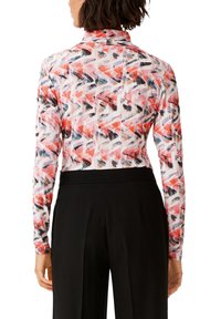 Długosleeve top z kolorowym geometrycznym wzorem w czerwonym, czarnym i białym kolorze. Wykonany z gładkiego materiału, o dopasowanym kroju.