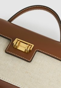 Pruun nahast käekott, mille esiküljel on kreemjat tekstuuriga kangas, kuldse tooni lukk ja valge õmblus servadel.