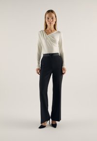 Long-sleeve, light cream top with a draped neckline paired with high-waisted black trousers, featuring a tailored fit and sleek design.