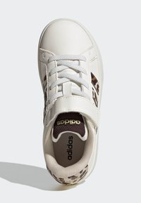 White leather sneaker featuring brown leopard print accents, flat white laces, and a padded interior with a gold logo on the tongue.