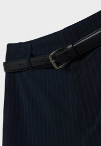 Pantalon bleu marine à rayures fines avec une ceinture en cuir noir dotée d'une boucle en métal argenté. Le tissu a une texture lisse.