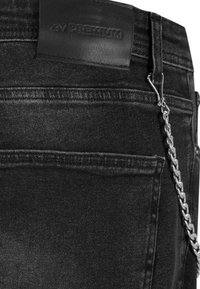 Pantalones vaqueros de mezclilla negra con una etiqueta de cuero en la cinturilla, un acento de cadena plateada y un diseño clásico de cinco bolsillos con costuras visibles.