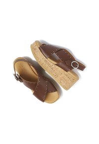 Bruine leren sandalen met kruislussen, studaccenten, kurken platform en verstelbare gespsluiting. Heeft een open teen en een rugbandontwerp.