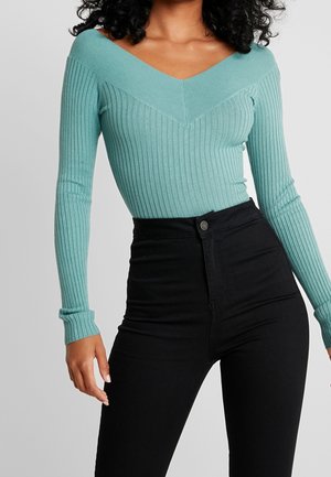 Turquoise ribbed long-sleeve top with a V-neck and fitted design, paired with high-waisted black jeans. Features textured fabric.