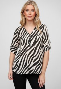 Black and beige zebra-striped blouse with a v-neckline, zipper detail, and rolled-up sleeves, made from smooth fabric.
